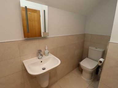 A bathroom with a wall-mounted sink and a toilet with a toilet paper holder at Oak Cottage in Lucker near Warenford
