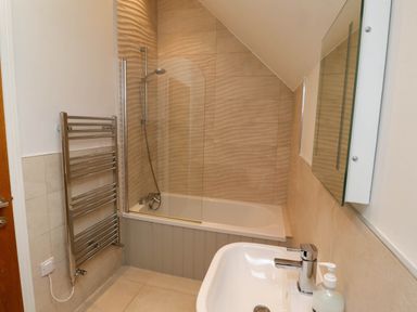 A bathroom with a bathtub and showerhead a towel rack a sink with a faucet and soap dispenser and a mirror at Oak Cottage in Lucker near Warenford