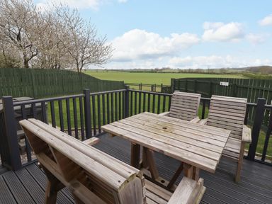 An outdoor wooden table with chairs on a deck overlooking a green fenced field at Oak Cottage in Lucker near Warenford