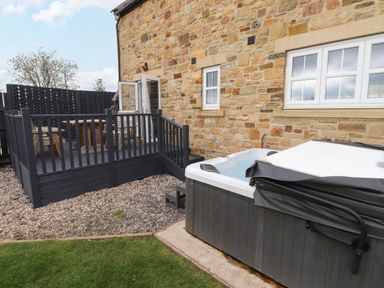 An outdoor patio area with a hot tub and a raised wooden deck with seating at Oak Cottage in Lucker near Warenford