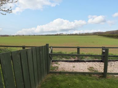 A green wooden fence and gate overlooking a grass field and cloudy sky at Oak Cottage in Lucker near Warenford
