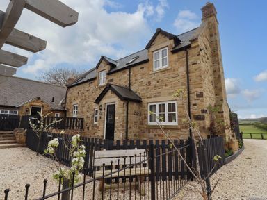A stone house with black picket fences and a bench on a gravel path at Oak Cottage in Lucker near Warenford