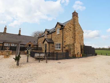 A stone cottage with two chimneys and a gravel yard at Oak Cottage in Lucker near Warenford