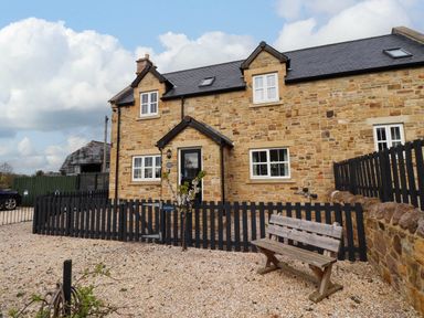 A stone house with black fencing and a wooden bench in the gravel front yard at Yew Cottage in Lucker near Warenford
