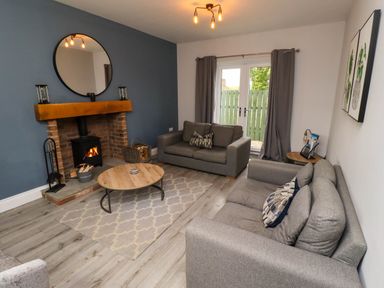 A living room with two gray sofas a round wooden coffee table a wood-burning stove and double glass doors at Yew Cottage in Lucker near Warenford