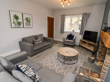 A living room with grey sofas a round wooden coffee table a TV on a wooden stand and a fireplace at Yew Cottage in Lucker near Warenford