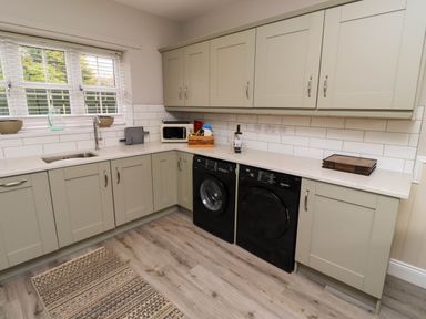 A kitchen with beige cabinets a countertop with a sink two black appliances and a window with blinds at Yew Cottage in Lucker near Warenford