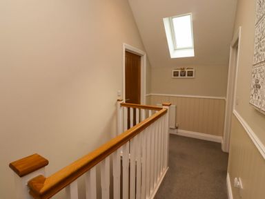 A hallway with carpeted floor wooden door railing with white spindles and a skylight window at Yew Cottage in Lucker near Warenford