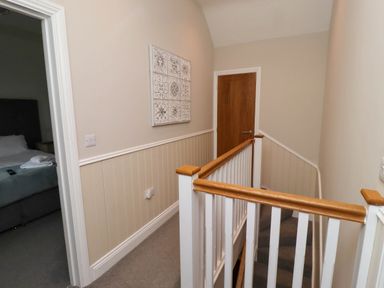 A hallway with a wooden door a staircase with white railing and a bedroom with a bed visible at Yew Cottage in Lucker near Warenford