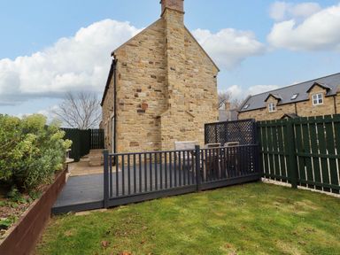 An outdoor patio with a table and chairs next to a stone house with a fenced garden at Yew Cottage in Lucker near Warenford