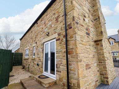 Stone exterior wall of a house with white double doors and small windows near a green wooden fence at Yew Cottage in Lucker near Warenford