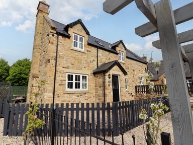 Stone house with black fence and small garden in front at Yew Cottage in Lucker near Warenford