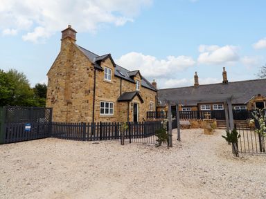 A stone house with black gates and fences and a gravel courtyard at Yew Cottage in Lucker near Warenford