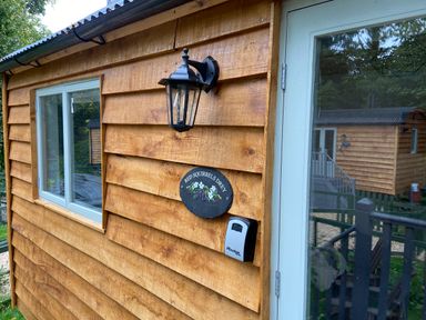 Exterior view of a wooden cabin with a window a black lantern a sign reading red squirrels drey and a keypad at Red Squirrels Drey Lucker near Belford