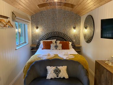 A bedroom with a bed with cushions and folded towels a sofa with a cushion a wall mirror and a television at Red Squirrels Drey in Lucker near Belford