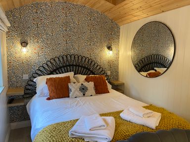 A bedroom with a bed with pillows and a yellow blanket a round mirror and patterned wallpaper at Red Squirrels Drey in Lucker near Belford