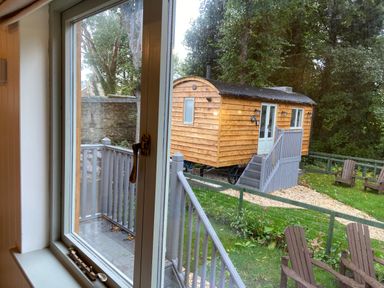 View through a window of a wooden shepherd hut with stairs leading to the door in a garden with chairs and grass at Red Squirrels Drey Lucker near Belford