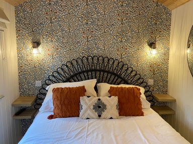 A bedroom with a double bed orange and patterned cushions wall lights and patterned wallpaper at Red Squirrels Drey Lucker near Belford