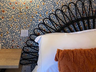 A bed with white pillow and orange cushion next to a wooden bedside table and patterned wallpaper at Red Squirrels Drey Lucker near Belford