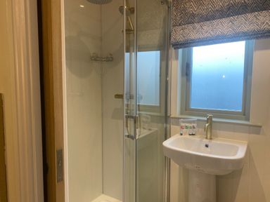A bathroom with a glass shower enclosure a white sink and a window with a patterned blind at Red Squirrels Drey in Lucker near Belford