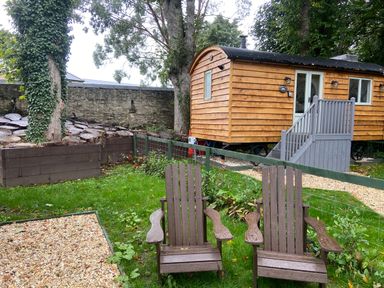A garden with two wooden chairs facing a wooden hut on wheels at Red Squirrels Drey in Lucker near Belford