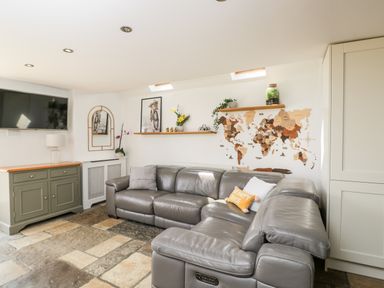 A living room with a gray leather sectional sofa TV on the wall and a world map on the wall at 2 Dewars Farm Cottages in Middleton Stoney