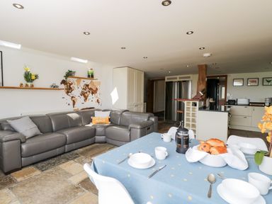 A kitchen and dining area with a gray sofa and a dining table set with dishes and pastries at 2 Dewars Farm Cottages in Middleton Stoney