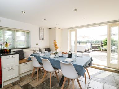 A dining area with a table set for breakfast and chairs next to sliding glass doors at 2 Dewars Farm Cottages in Middleton Stoney