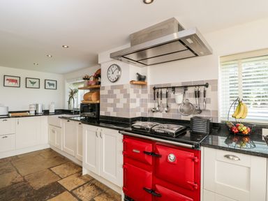 A kitchen with white cabinets a red stove black countertops and utensils hanging on the wall at 2 Dewars Farm Cottages in Middleton Stoney
