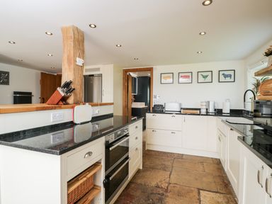 A kitchen with black countertops white cabinets a wooden support beam and framed animal prints on the wall at 2 Dewars Farm Cottages in Middleton Stoney