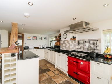 A kitchen with white cabinets a red stove and black countertops at 2 Dewars Farm Cottages in Middleton Stoney