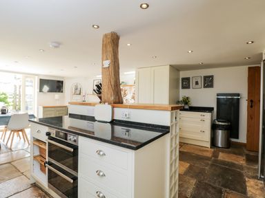 A kitchen with a black countertop island oven white cabinets wooden beam and a dining area at 2 Dewars Farm Cottages in Middleton Stoney