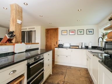 A kitchen with white cabinets black countertops and framed animal prints on the wall at 2 Dewars Farm Cottages in Middleton Stoney