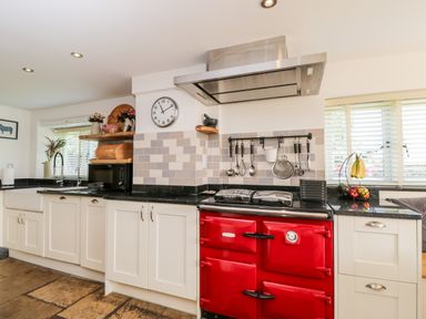 A kitchen with white cabinets a red stove a black countertop and kitchen utensils hanging on the wall at 2 Dewars Farm Cottages in Middleton Stoney