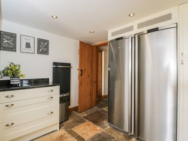 A kitchen area with stainless steel refrigerator units wooden door stone tile floor and white cabinets at 2 Dewars Farm Cottages in Middleton Stoney