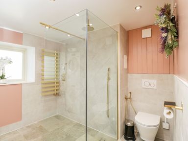 A bathroom with a glass shower enclosure a toilet with gold fixtures and a floral arrangement on the wall at 2 Dewars Farm Cottages in Middleton Stoney