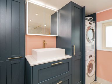 A laundry room with stacked washer and dryer a white sink with a gold faucet and navy blue cabinets at 2 Dewars Farm Cottages in Middleton Stoney