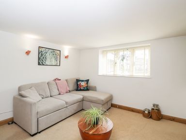 A living room with a beige sofa a wooden coffee table with a plant and wall art at 2 Dewars Farm Cottages in Middleton Stoney