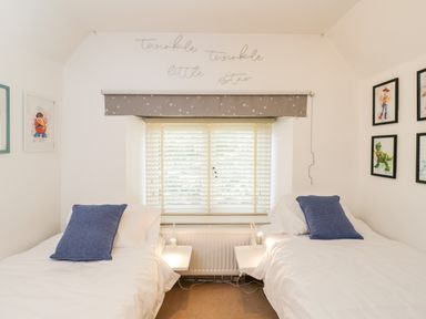 A bedroom with two single beds and blue pillows by a window with blinds at 2 Dewars Farm Cottages in Middleton Stoney