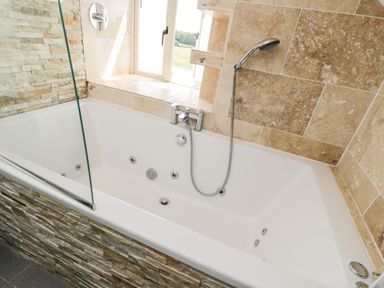 A bathtub with a handheld shower head and tiled walls at 2 Dewars Farm Cottages in Middleton Stoney