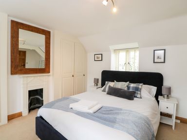A bedroom with a double bed pillows bedside tables lamps a mirror above a fireplace and built in wardrobes at 2 Dewars Farm Cottages in Middleton Stoney