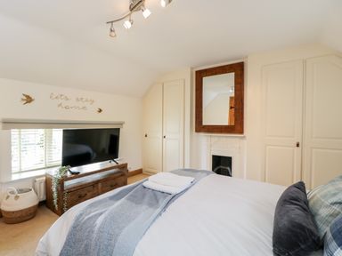 A bedroom with a bed pillows a television on a wooden cabinet built in wardrobes and a mirror above a fireplace at 2 Dewars Farm Cottages in Middleton Stoney