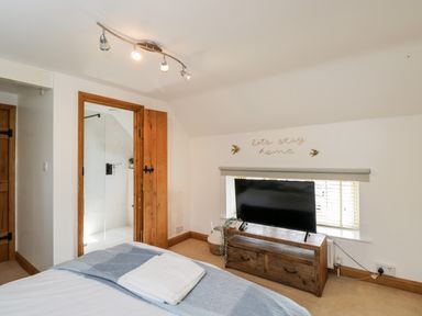 A bedroom with a bed a wooden TV stand with a television and an open door to a bathroom at 2 Dewars Farm Cottages in Middleton Stoney