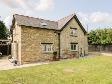 An exterior view of a stone house with windows and a grassy lawn at 2 Dewars Farm Cottages in Middleton Stoney