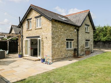 A stone house with an open double door leading to a patio with scooters and a dining area at 2 Dewars Farm Cottages in Middleton Stoney