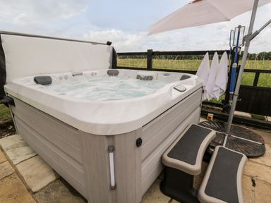 An outdoor hot tub with water jets and a cover propped open near a field at 2 Dewars Farm Cottages in Middleton Stoney