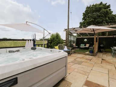 An outdoor patio with a hot tub umbrellas seating area and trees at 2 Dewars Farm Cottages in Middleton Stoney