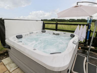 An outdoor hot tub with bubbling water and headrests next to a fence with a field and trees in the background at 2 Dewars Farm Cottages Middleton Stoney