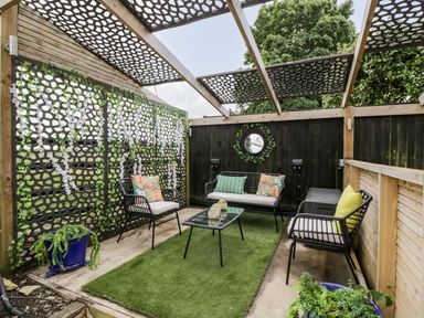 An outdoor seating area with metal chairs and a sofa around a glass table on a green rug at 2 Dewars Farm Cottages in Middleton Stoney