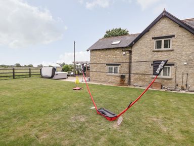 A backyard with a badminton net set up on the grass and a stone house in the background at 2 Dewars Farm Cottages Middleton Stoney